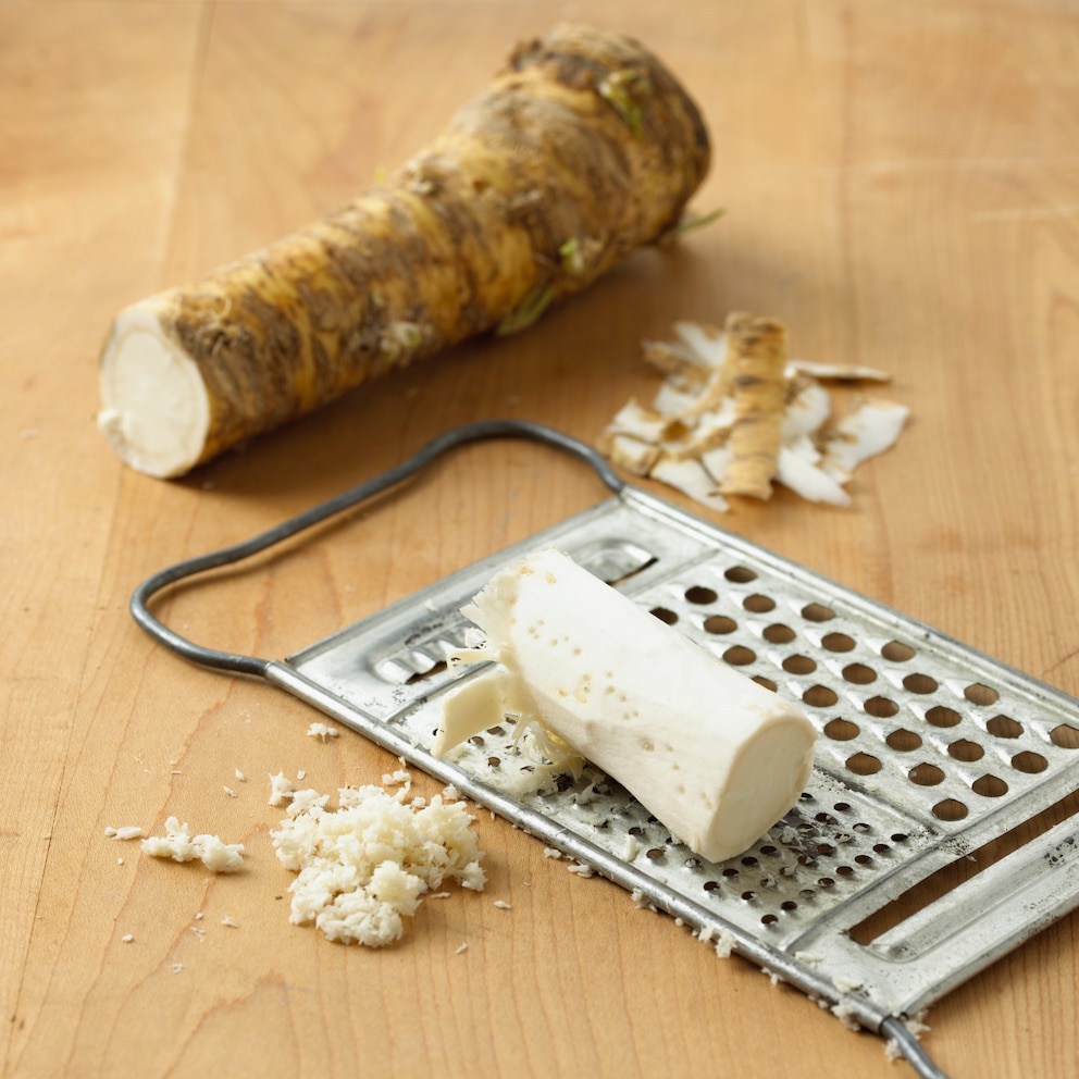 Meerrettich liegt mit einer Reibe auf einem Holztisch