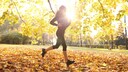 Eine junge Frau joggt in der Herbstsonne durch einen Park