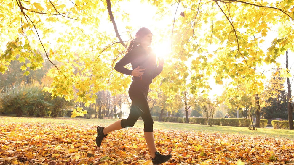 Eine junge Frau joggt in der Herbstsonne durch einen Park