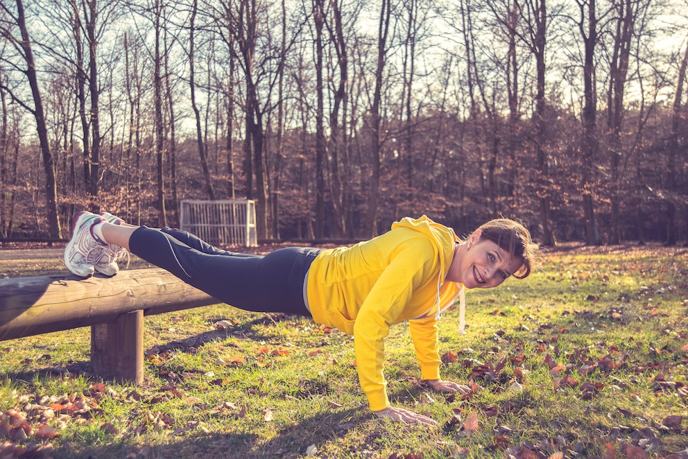 Eine Frau macht Push-ups (Liegestütze) mit Hilfe einer Bank in einem Park