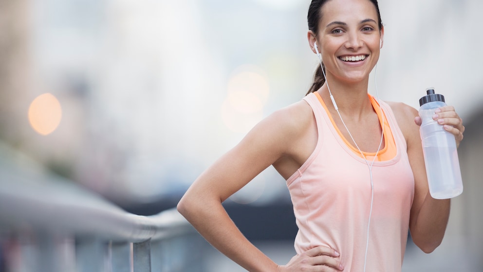 Ist Training auf nüchternem Magen besser? Eine junge Frau trinkt in Sportkleidung aus einer Flasche Wasser