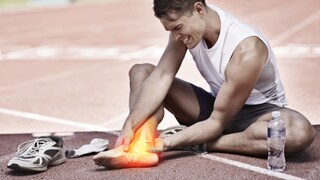 Sport und Gelenkschmerzen: Ein junger Mann sitzt auf einer Laufbahn und hält sich seinen schmerzenden Fuß