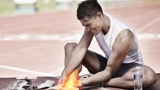 Sport und Gelenkschmerzen: Ein junger Mann sitzt auf einer Laufbahn und hält sich seinen schmerzenden Fuß