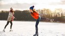 Zwei junge Frauen beim Schlittschuhlaufen auf einem See in der Sonne