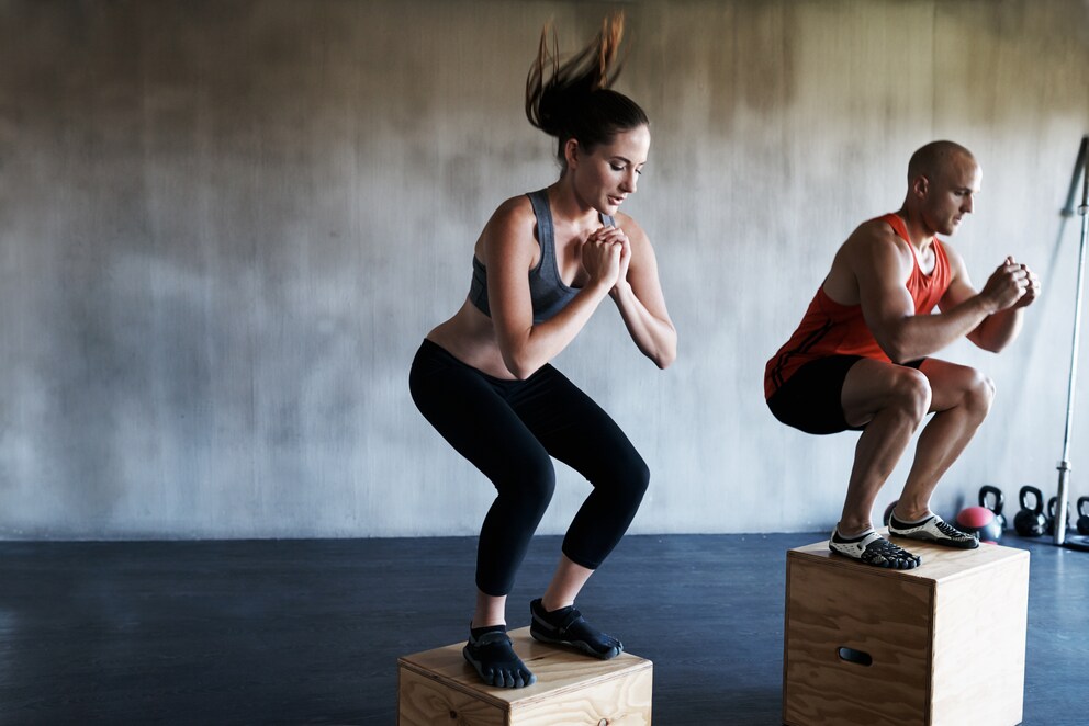 A woman and a man doing box jumps in a gym