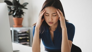 Eine junge Frau sitzt im Büro und leidet an Migräne