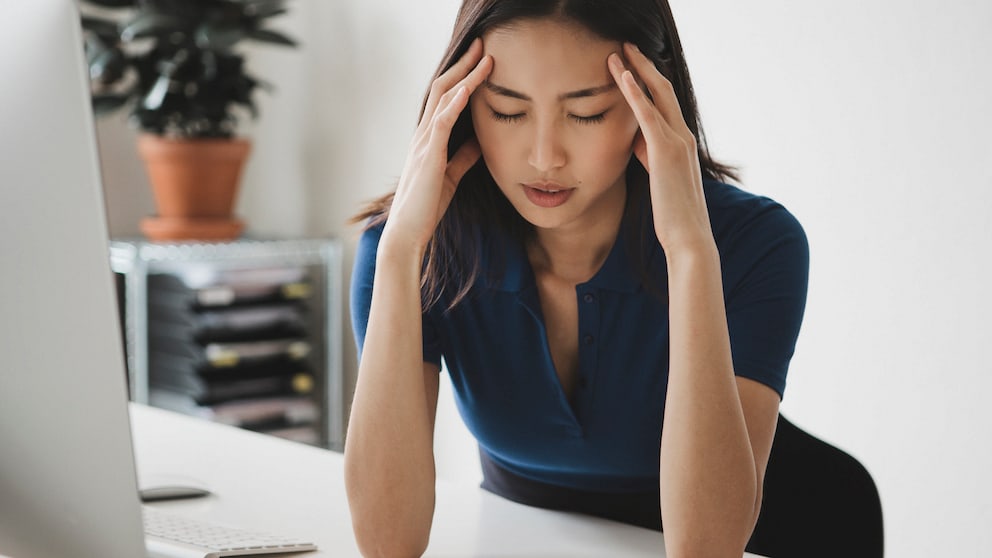 Eine junge Frau sitzt im Büro und leidet an Migräne