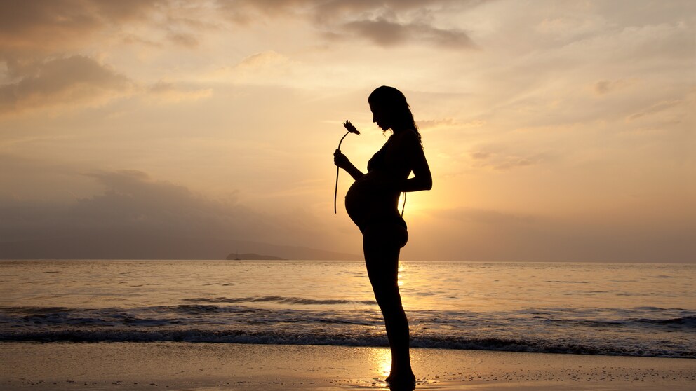 Eine Schwangere steht am Strand während des Sonnenuntergangs