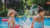 Zwei Kinder planschen mit den Beinen im Schwimmbecken