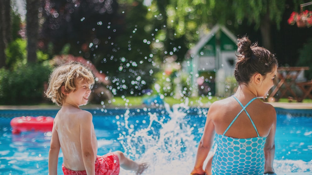 Zwei Kinder planschen mit den Beinen im Schwimmbecken