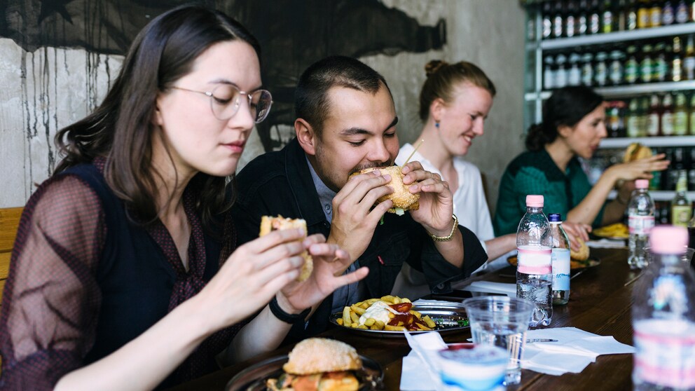 Junge Menschen beißen mit offensichtlichem Genuss in einen Burger