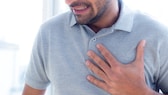 Ein Mann hält mit schmerzverzehrtem Gesicht seine Hand an die linke Brust