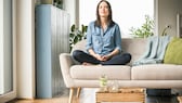 Eine Frau meditiert auf dem Sofa