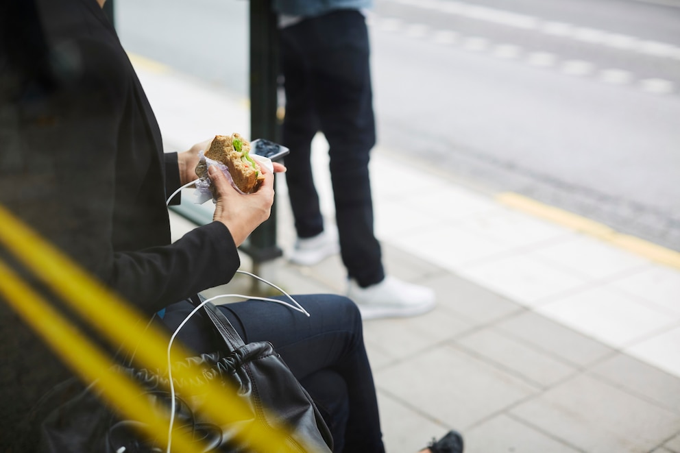 Frau isst an der Bushaltestelle ein Brötchen