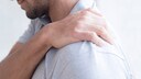 Mann fasst seine schmerzende Schulter an