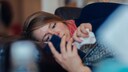 Corona-Verdacht: Eine kranke Frau liegt auf dem Sofa und hält ein Smartphone in der Hand