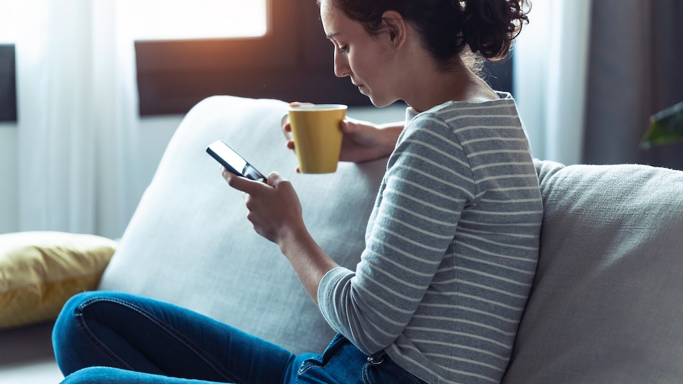 Eine junge Frau mit Smartphone auf der Couch