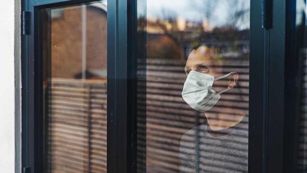 Mann mit Mundschutz hinter einem Fenster