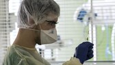 Impfstoff: Ein Mediziner in Schutzkleidung und mit Mund-Nasen-Schutzmaske hält eine aufgezogene Spritze hoch