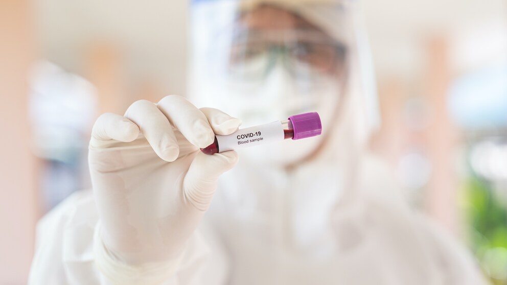 Mutation: Ein Mann in Schutzanzug hält eine Blutprobe in der Hand