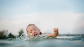 Ein Kind versucht sich beim Baden im See über Wasser zu halten