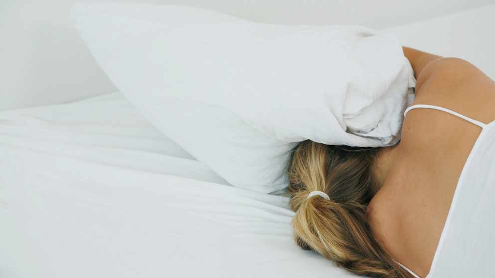 Straßenlärm: Eine Frau hält sich im Bett die Ohren mit einem Kissen zu