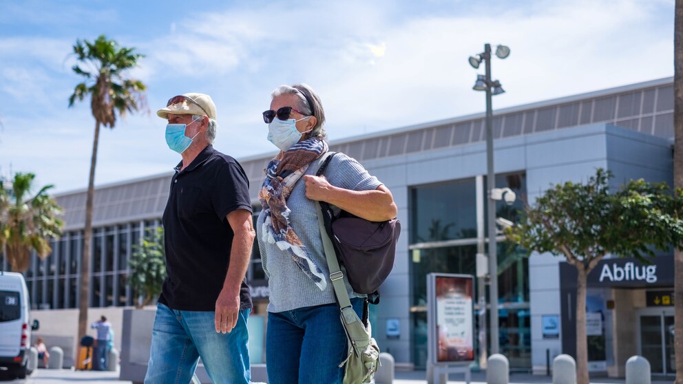 Zwei Urlauber mit Maske vor dem Flughafen