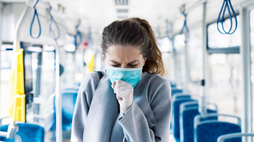 trockene Luft Corona-Infektionen: Eine Frau hustet in ihren Mund-Nasen-Schutz