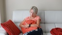 Eine Frau sitzt traurig auf dem Sofa und umklammert ein Kissen