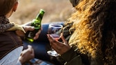 Frau und Mann trinken Rotwein oder Bier – was ist gesünder?