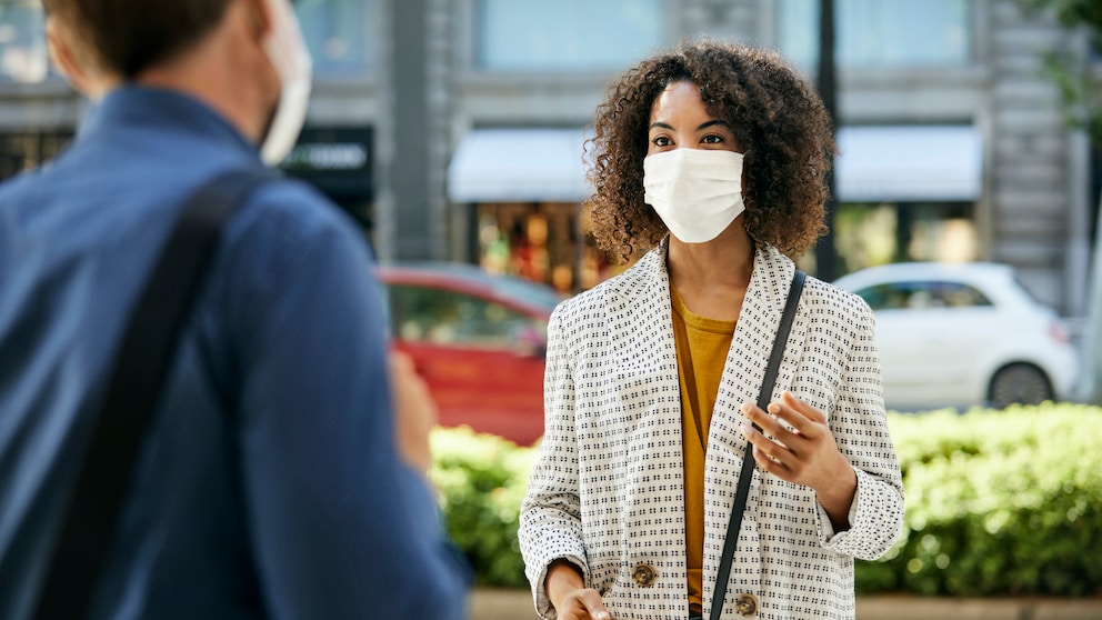 Eine Frau trägt eine Maske und unterhält sich mit einer anderen Person