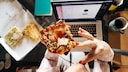 Fettleibigkeit: Eine Frau ist vor einem Laptop ein Stück Pizza