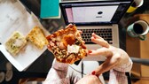 Fettleibigkeit: Eine Frau ist vor einem Laptop ein Stück Pizza