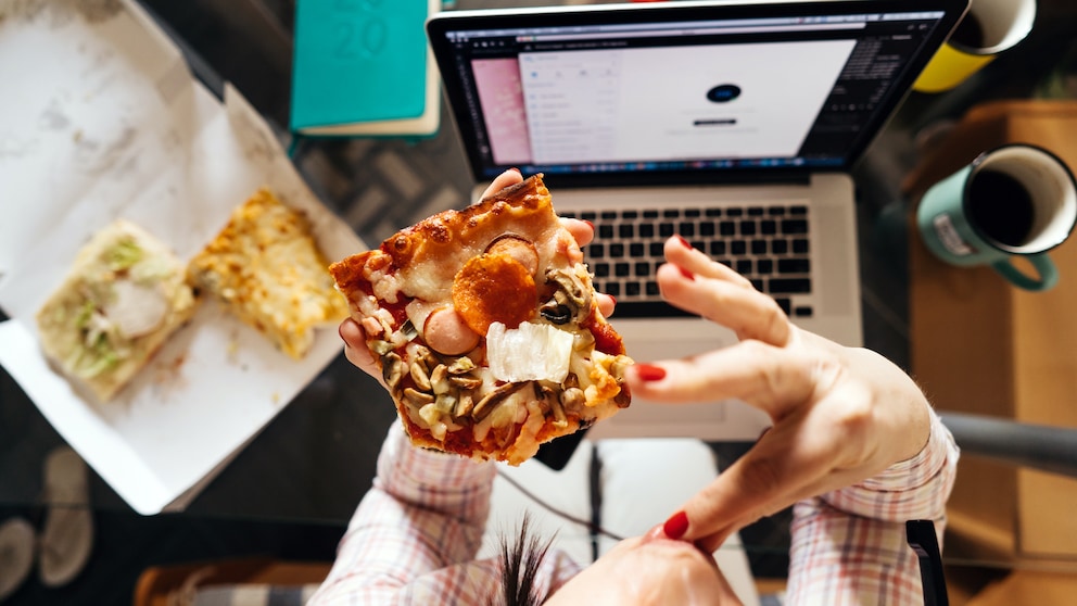 Fettleibigkeit: Eine Frau ist vor einem Laptop ein Stück Pizza