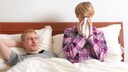 Niesen Sex: Ein Paar liegt im Bett, der Mann schaut die Frau an, w&auml;hrend sie niest