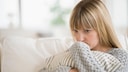 Eine junge Frau sitzt traurig auf dem Sofa