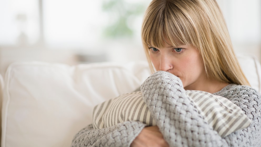 Eine junge Frau sitzt traurig auf dem Sofa