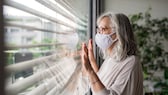 Frau mit Mundschutz am Fenster