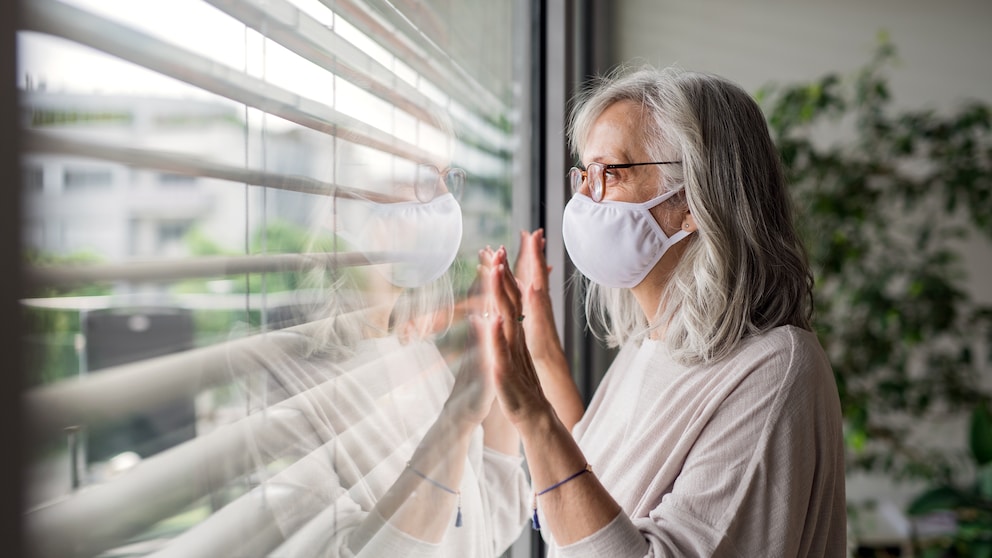 Frau mit Mundschutz am Fenster