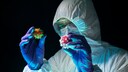 Ein Wissenschaftler im Schutzanzug hält symbolhafte Coronaviren in den Händen