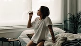 Frau sitzt im Bett und trinkt ein Glas Wasser