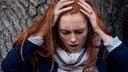Eine rothaarige Frau h&auml;lt sich vor Schmerzen den Kopf