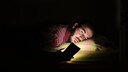 Mann schaut im Bett aufs Handy