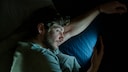 Ein Mann schaut im Bett aufs Smartphone