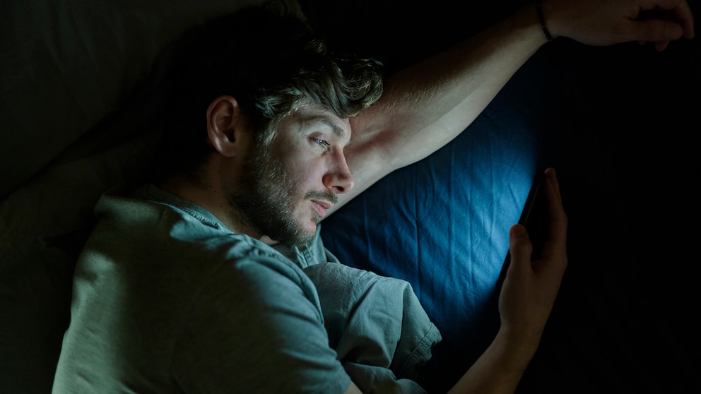 Ein Mann schaut im Bett aufs Smartphone