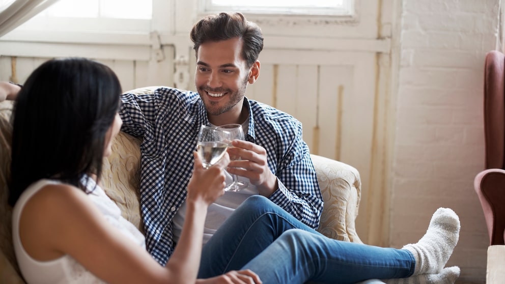 Ein junges Paar sitzt auf dem Sofa und trinkt Weißwein