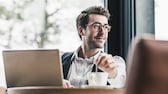 Junger Mann sitzt vor dem Laptop mit einer Tasse Kaffee