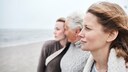 Zwei junge Frauen gehen mit ihrer Mutter am Strand spazieren