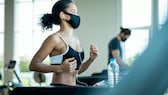 Frau joggt im Fitnessstudio mit Maske auf dem Laufband