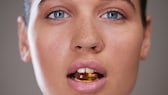 Eine Frau mit einer Supplement-Kapsel zwischen den Zähnen